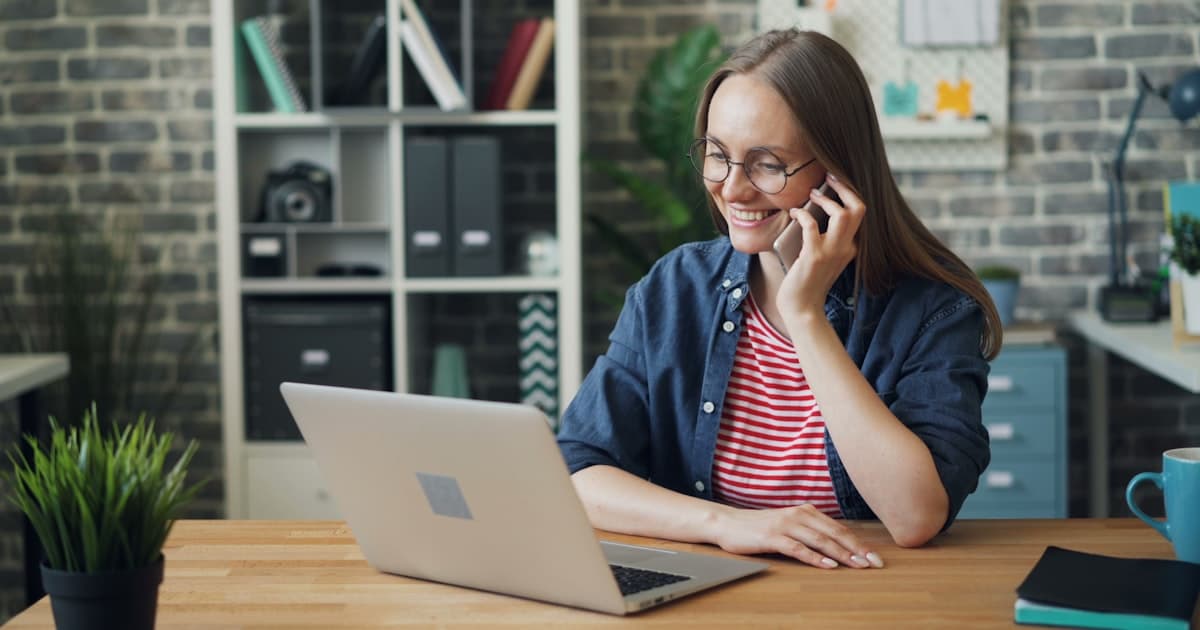a woman talking on a cell phone while using a laptop